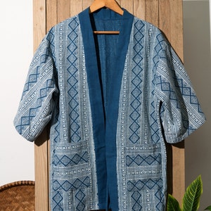 May include: A blue and white patterned kimono with a tie closure. The kimono is hanging on a wooden hanger against a wooden background.