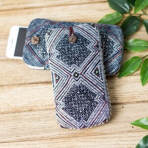 May include: Two blue and white patterned fabric phone cases with a wooden button closure. The cases are on a wooden surface with green leaves.