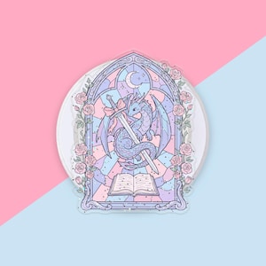 Puede incluir: Una pegatina de colores pastel con un dragón sosteniendo una espada, dentro de un diseño de vidriera. El dragón es azul claro con alas moradas, una espada y un lazo rosa. Rosas y una luna creciente decoran el borde. Un libro abierto en la parte inferior.