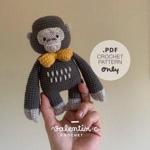 May include: A crocheted gray gorilla toy with a yellow bow tie. The toy is being held in a hand. The text '.PDF CROCHET PATTERN only' is visible in the image.