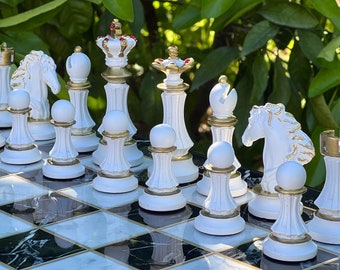 May include: A white and gold chess set with pieces arranged on a black and white marble chessboard. The pieces are made of ceramic and have a glossy finish.