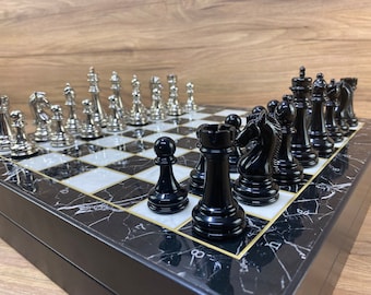 May include: A black and white marble chessboard with silver chess pieces on one side and black chess pieces on the other side. The board is set up for a game of chess.