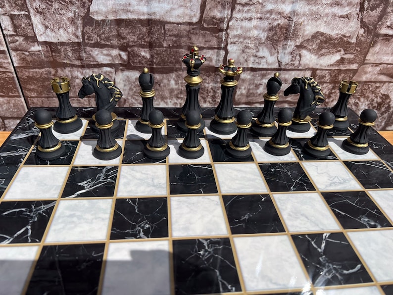 May include: A black and gold chess set with black and white marble board. The chess pieces are arranged in the starting position for a game of chess.