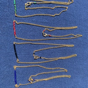 May include: Five gold chain necklaces with different colored beads. The beads are in a line and are turquoise, red, black, blue, and blue.