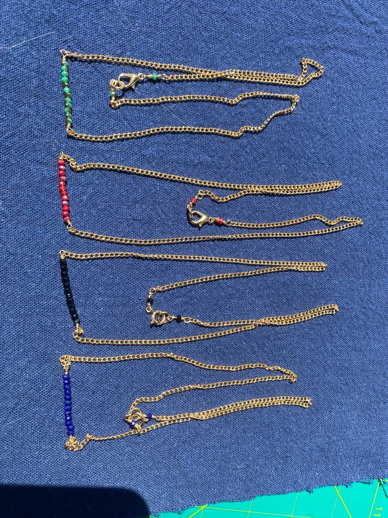 May include: Five gold chain necklaces with different colored beads. The beads are in a line and are turquoise, red, black, blue, and blue.