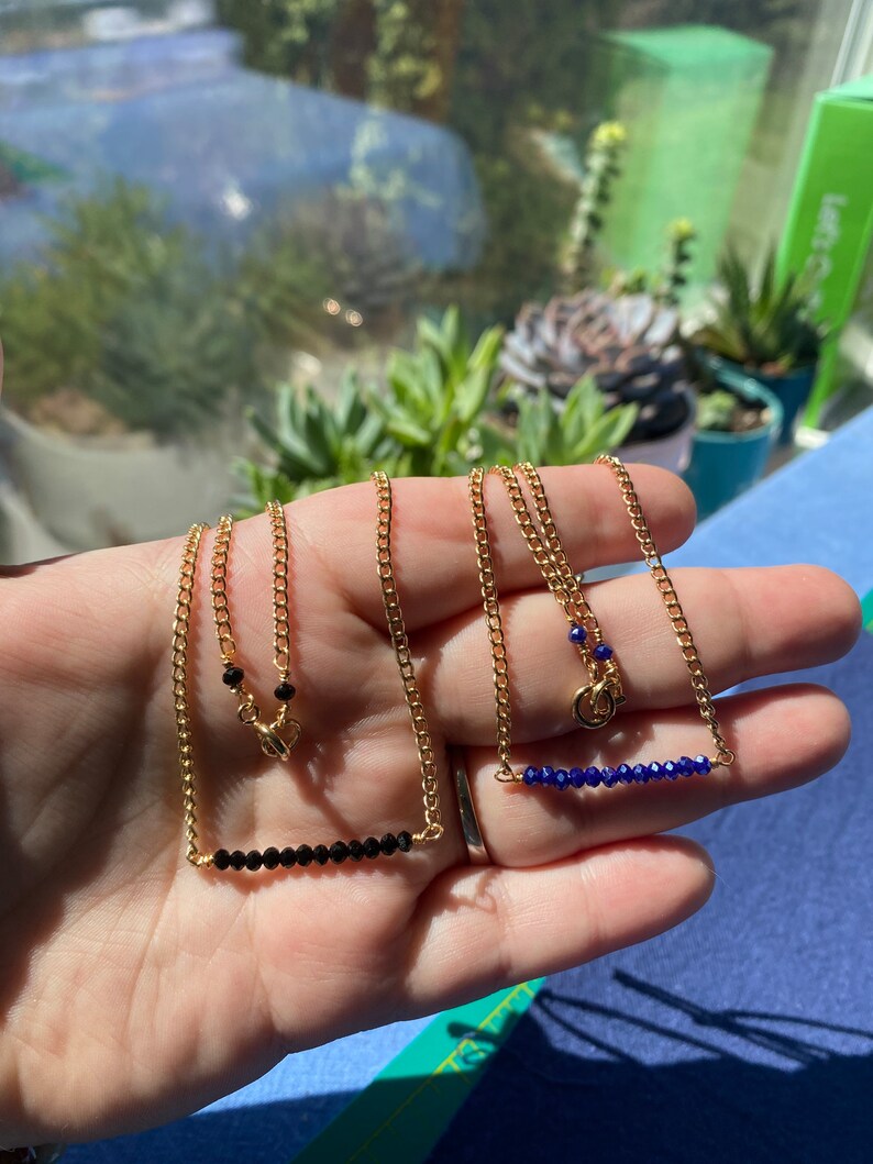 May include: Two gold chain necklaces with a bar of gemstones. One necklace has black gemstones and the other has blue gemstones.