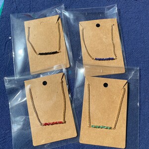 May include: Four gold chain necklaces with different colored beads. Each necklace is displayed on a brown card with a hole at the top for hanging.