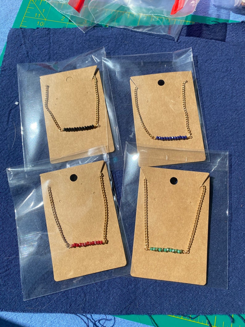 May include: Four gold chain necklaces with different colored beads. Each necklace is displayed on a brown card with a hole at the top for hanging.