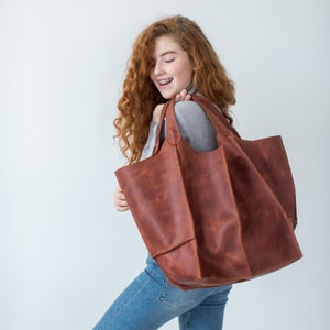 May include: A large brown leather tote bag with a zipper closure. The bag has a wide opening and two long handles.