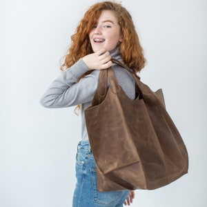 May include: A brown leather tote bag with a wide opening and two handles. The bag is large enough to carry a lot of items.