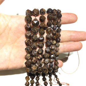 Puede incluir: Una hebra de cuentas de piedra preciosa facetadas de color marrón y dorado. Las cuentas tienen forma de pirámide con muchos lados. Las cuentas están enhebradas en un cordón fino marrón.