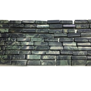 May include: A close-up of a row of green and black patterned rectangular gemstone beads. The beads are arranged in a brick-like pattern.