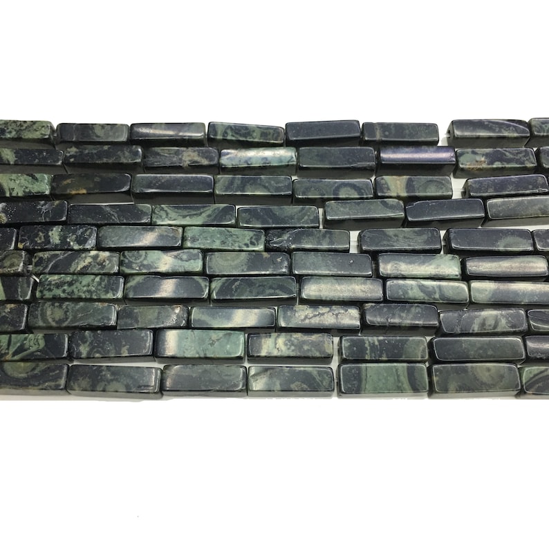 May include: A close-up of a row of green and black patterned rectangular gemstone beads. The beads are arranged in a brick-like pattern.