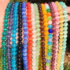 May include: Assortment of colorful glass beads with a cat's eye effect. The beads are round and have a smooth, polished finish. The colors include blue, green, red, white, yellow, and purple.