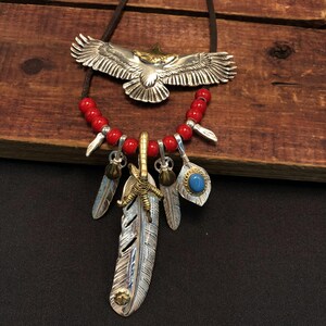 May include: A silver eagle pendant necklace with red beads and silver feather charms. The eagle is spread-winged and has a gold head. The necklace also features a silver claw charm and a turquoise stone charm.
