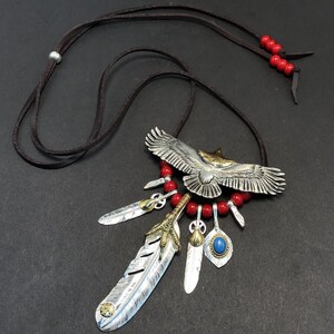 May include: Silver eagle pendant necklace with red beads, feathers, and a turquoise stone. The eagle is spread-winged and has a gold accent on its head.