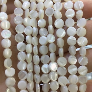 May include: A strand of white round shell beads with iridescent shimmer. The beads are approximately 10mm in diameter.