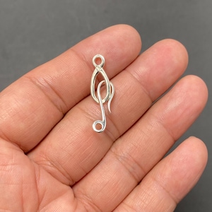 Puede incluir: Un pequeño colgante plateado con forma de clave de sol. El colgante es una representación estilizada de una nota musical, con un lazo en la parte superior para colgarlo. El diseño es simple y elegante, para amantes de la música.