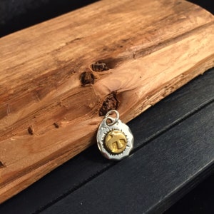 K&ouml;nnte beinhalten: Ein ovaler Anh&auml;nger aus Silber und Gold mit einem Vogelmotiv. Der Anh&auml;nger hat eine strukturierte Oberfl&auml;che.