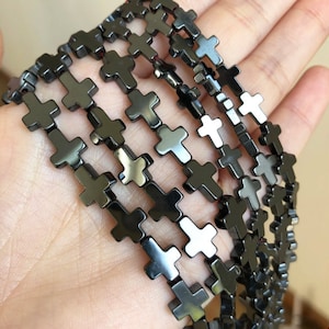 May include: A strand of black cross-shaped beads. The beads are made of polished black hematite and are approximately 10mm in size.