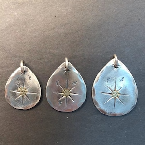 May include: Three silver teardrop-shaped pendants with a starburst design and a small gold dot in the center. Each pendant has a small loop at the top for attaching a chain.