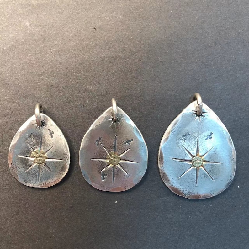 May include: Three silver teardrop-shaped pendants with a starburst design and a small gold dot in the center. Each pendant has a small loop at the top for attaching a chain.