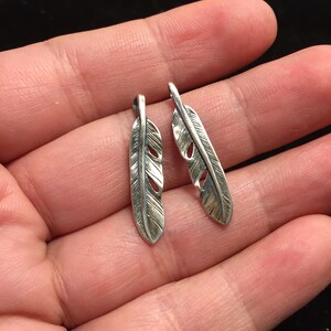 Puede incluir: Dos abalorios de plata en forma de pluma con un dise&ntilde;o detallado. Las plumas tienen un dise&ntilde;o recortado y miden aproximadamente 5 cm de largo.