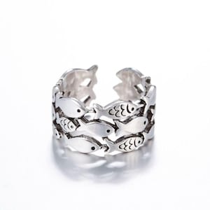 May include: A silver ring with a design of multiple fish swimming around the band.