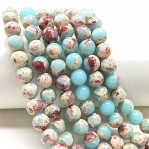 May include: A strand of round, blue and white jasper beads with red and brown marbling. The beads are approximately 10mm in diameter.