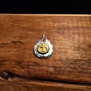 K&ouml;nnte beinhalten: Ein silberner Anh&auml;nger mit geh&auml;mmerter Textur und einem goldfarbenen Vogel-Anh&auml;nger in der Mitte.