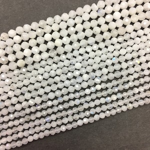 May include: A strand of white moonstone beads, each bead is faceted and has a round shape. The beads are strung on a clear thread.