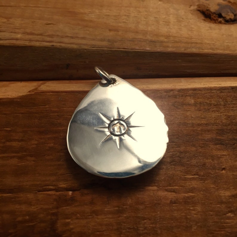 May include: A silver teardrop-shaped pendant with a starburst design and a small gold circle in the center.