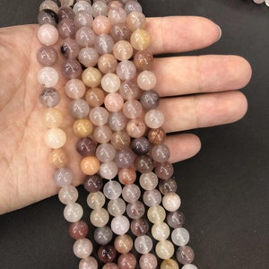 Puede incluir: Una hebra de cuentas redondas de piedra preciosa translúcidas en tonos rosa, marrón y blanco. Las cuentas están enhebradas en un cordón elástico transparente y tienen un diámetro aproximado de 8 mm.