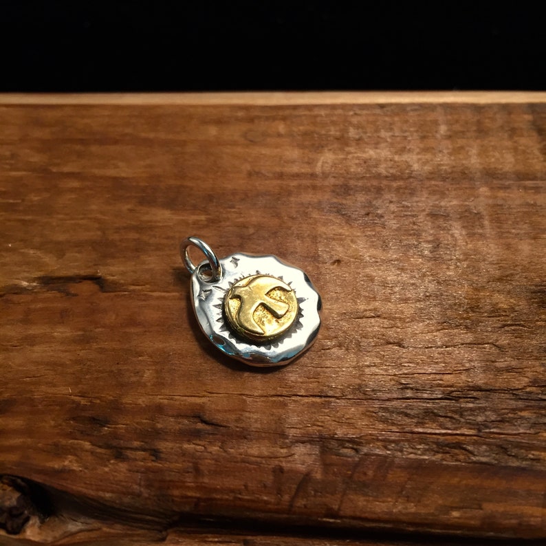 K&ouml;nnte beinhalten: Ein silberner Anh&auml;nger mit geh&auml;mmerter Textur und einem goldfarbenen Friedenszeichen-Anh&auml;nger.