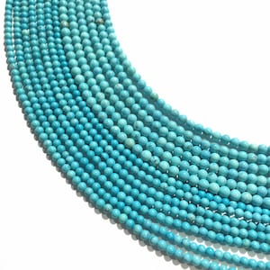 Op de afbeelding: Een streng turquoise kralen, elke kraal is rond en glad. De kralen zijn lichtblauw en zijn gerangschikt in een gebogen patroon.