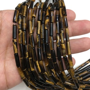 Könnte beinhalten: Eine Strähne Tigerauge-Perlen, jede Perle hat eine längliche, rechteckige Form mit einer goldbraunen Farbe und schwarzen Streifen. Die Perlen sind zu einer langen Halskette aufgereiht.