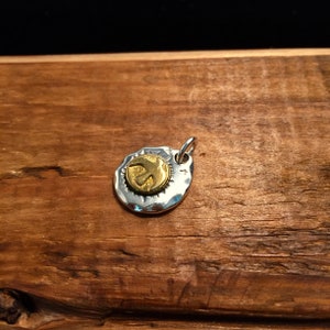 K&ouml;nnte beinhalten: Ein silberner Anh&auml;nger mit geh&auml;mmerter Textur und einem goldfarbenen Friedenszeichen-Anh&auml;nger.