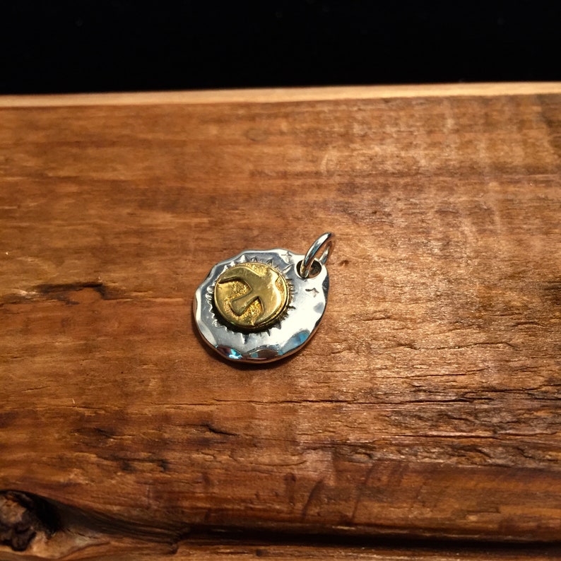 K&ouml;nnte beinhalten: Ein silberner Anh&auml;nger mit geh&auml;mmerter Textur und einem goldfarbenen Friedenszeichen-Anh&auml;nger.