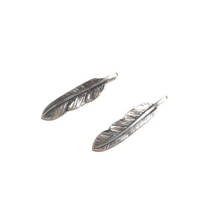 Puede incluir: Dos abalorios de plumas de plata con dise&ntilde;os de plumas detallados.