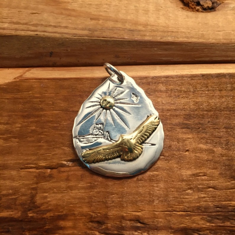 May include: Silver teardrop pendant with a gold eagle in flight, a sun with rays, and a small image of a lighthouse.