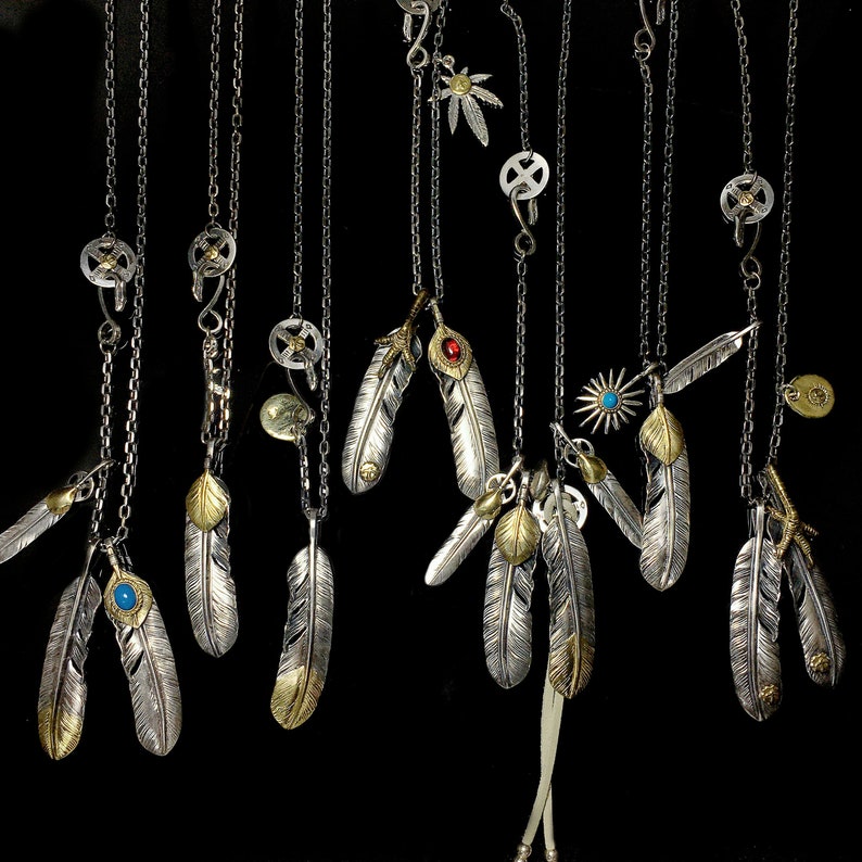 May include: A collection of silver necklaces with feather pendants. The feathers are detailed and have a variety of finishes, including gold and turquoise accents.