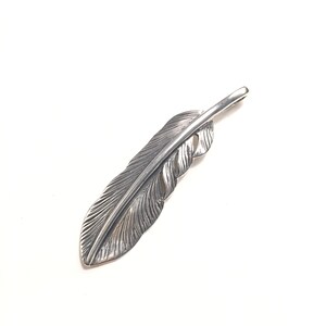 May include: A silver-colored feather pendant with detailed veining. The pendant is a stylized representation of a feather, with a loop at the top for a chain. The feather is set against a white background.