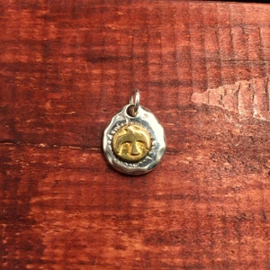 K&ouml;nnte beinhalten: Ein silberner Anh&auml;nger mit geh&auml;mmerter Textur zeigt im Zentrum ein goldenes Vogelmotiv. Der Anh&auml;nger ist oval geformt und hat oben eine &Ouml;se zum Anbringen einer Kette.