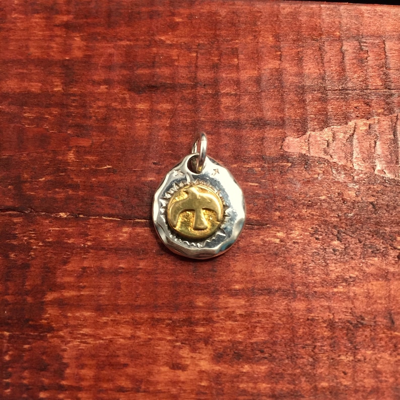 K&ouml;nnte beinhalten: Ein silberner Anh&auml;nger mit geh&auml;mmerter Textur zeigt im Zentrum ein goldenes Vogelmotiv. Der Anh&auml;nger ist oval geformt und hat oben eine &Ouml;se zum Anbringen einer Kette.