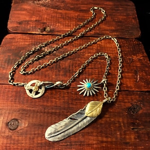 May include: A silver chain necklace with a silver and gold feather pendant, a silver sunburst pendant with a turquoise stone, and a silver circular pendant with a compass design.