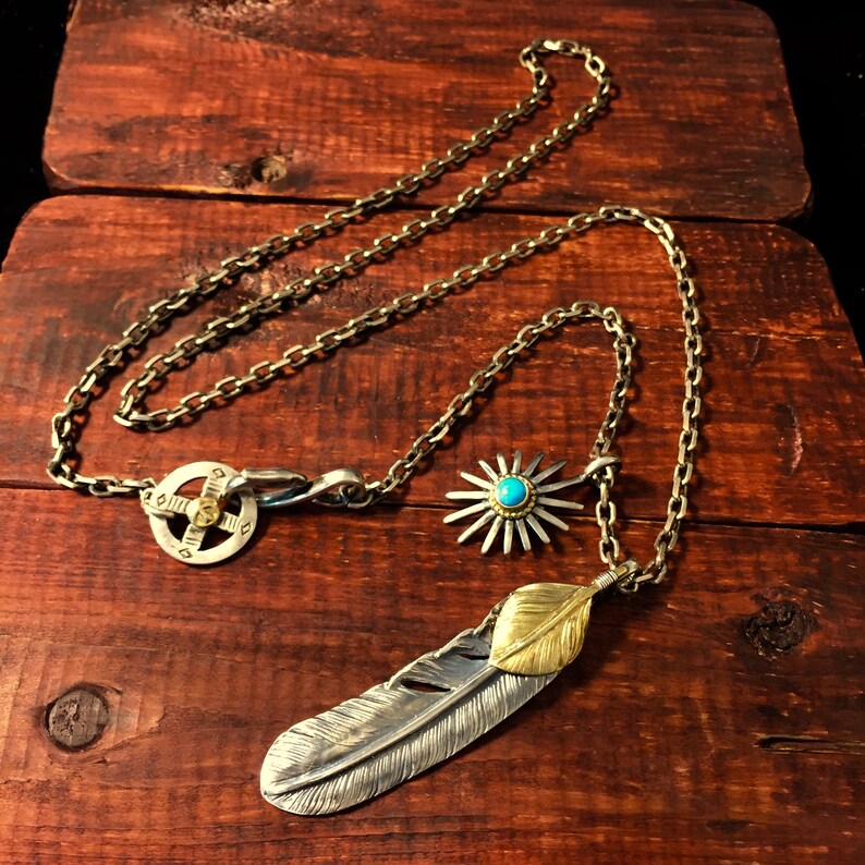 May include: A silver chain necklace with a silver and gold feather pendant, a silver sunburst pendant with a turquoise stone, and a silver circular pendant with a compass design.