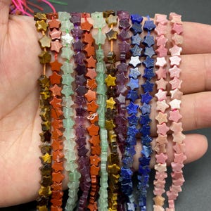 Puede incluir: Cadenas de cuentas en forma de estrella en varios colores, incluyendo marrón, naranja, verde, morado, azul y rosa. Las cuentas están ensartadas en finos cordones, creando una exhibición colorida y texturizada. Las estrellas son pequeñas y bien definidas.