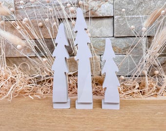 May include: Three gray wooden Christmas tree ornaments of varying sizes. The trees are simple and modern in design.