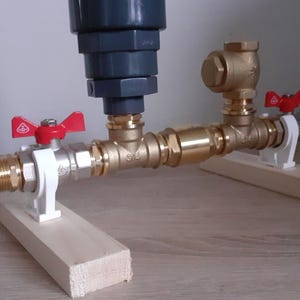 May include: A plumbing system with two brass valves and a gray filter. The valves have red handles and are mounted on wooden supports.