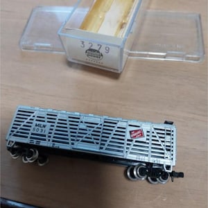 以下が含まれることがあります： 黒い車輪と「MILW 5031」の文字が入ったシルバーの模型列車。 車両はスラットデザインで、「THE MILWAUKEE ROAD」と書かれた赤と白のロゴが付いています。 背景には「3279」の文字が入った透明なプラスチックケースがあります。